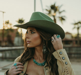 Woman wearing a green hat and beige jacket with fringe, standing outdoors.